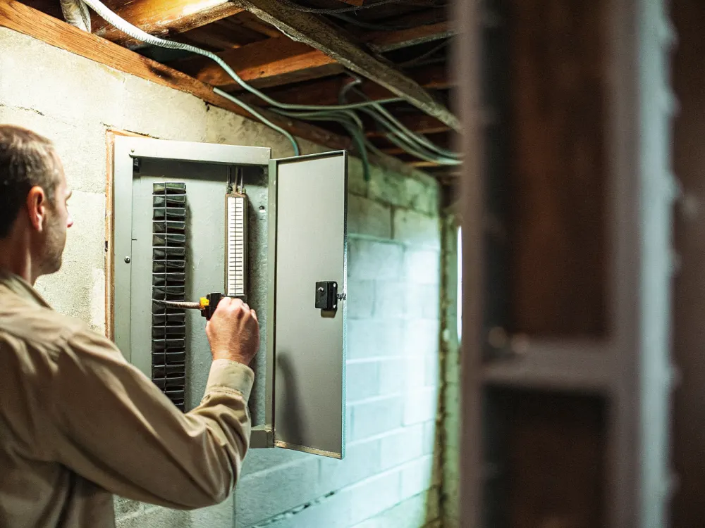 Bayline electrician at an open electrical panel checking it with a multimeter